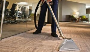 A man is using a vacuum cleaner to clean a carpet in an office.