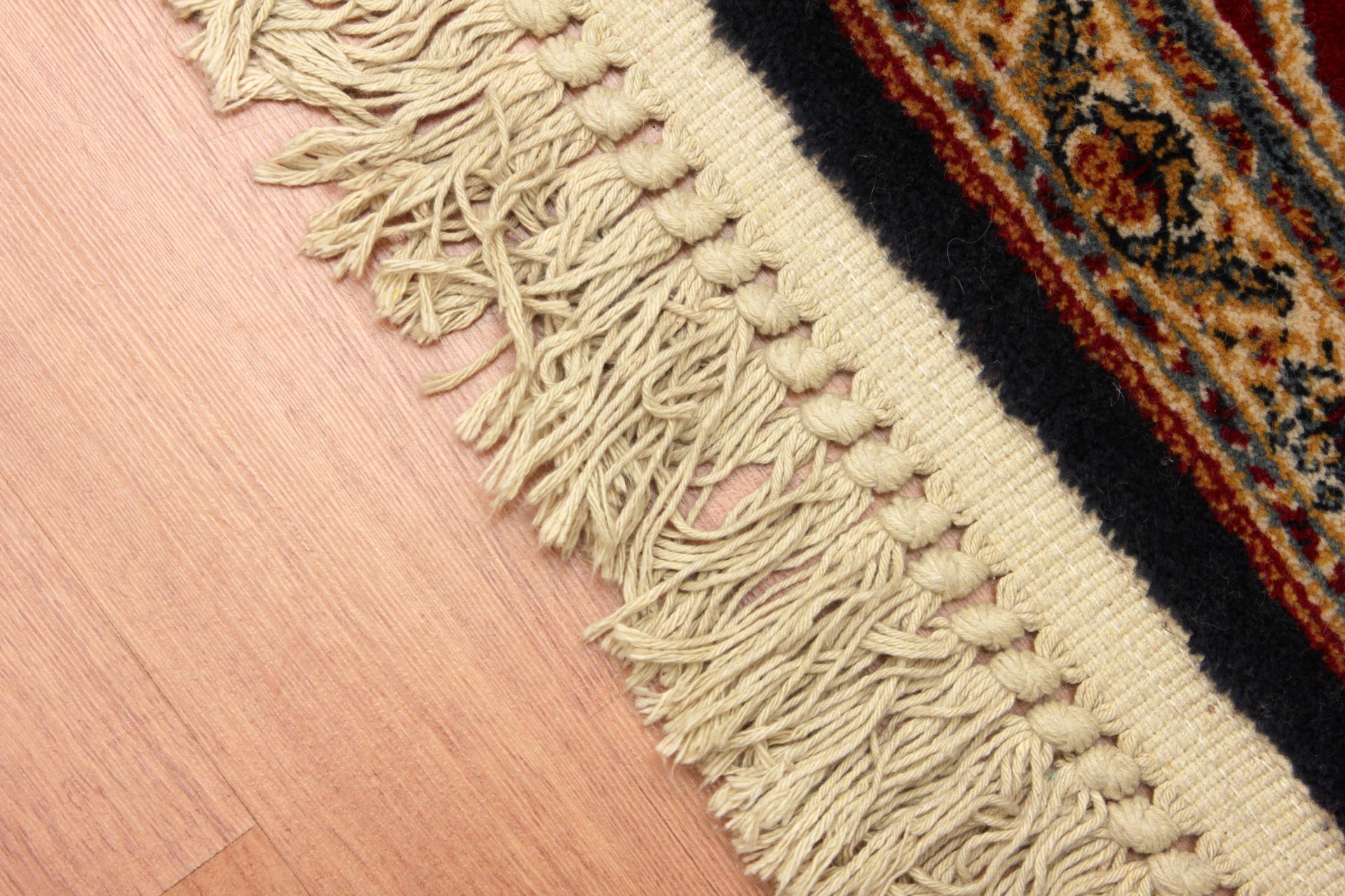 A close-up of a rug with fringe on a wooden floor.