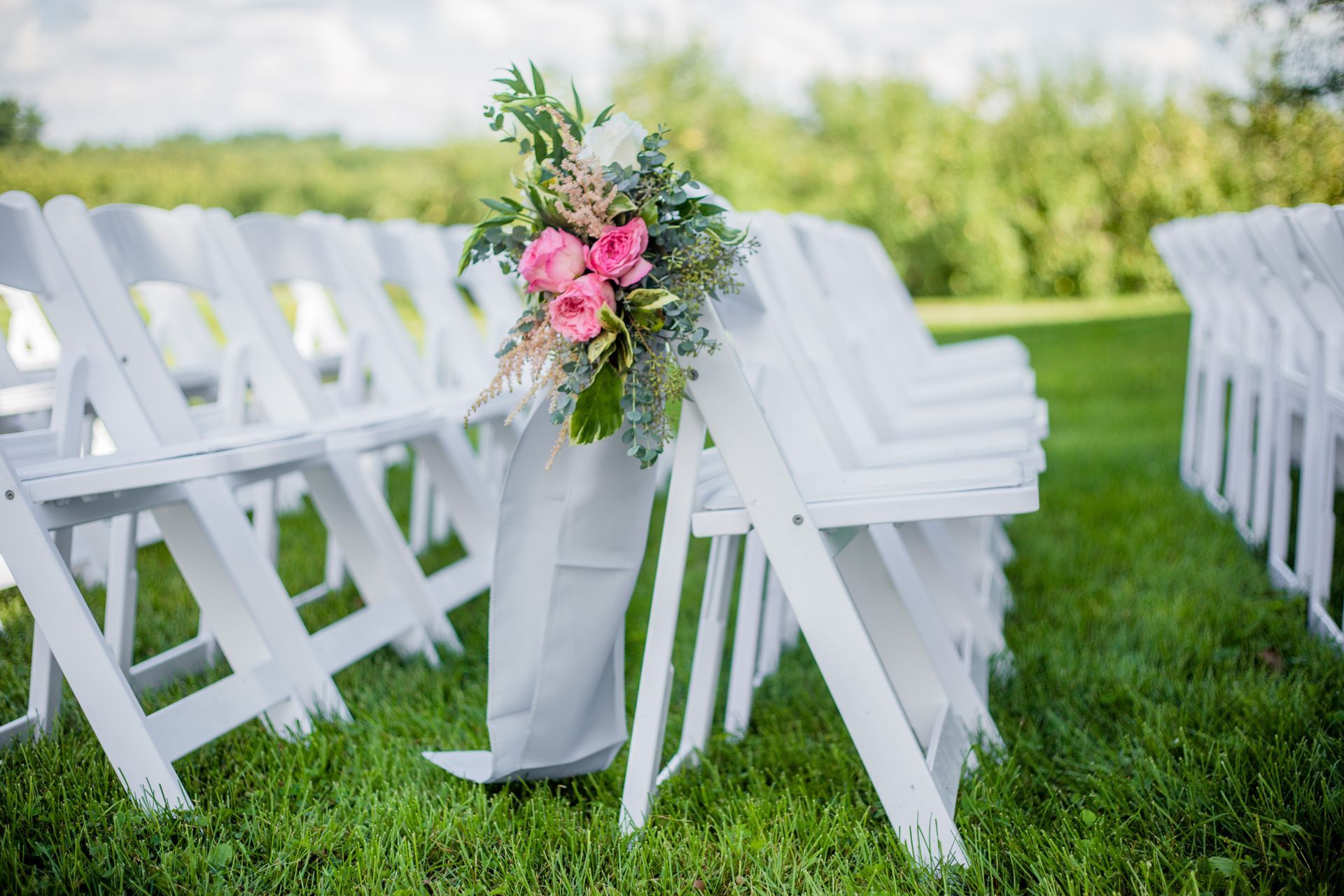 Rows of white chairs in a field decorated with pink flowers and greenery
