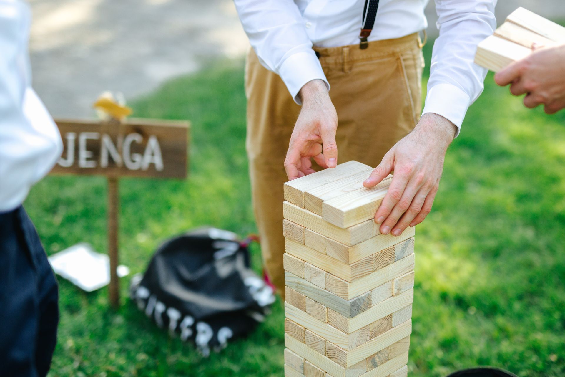 People playing Jenga outdoors; one removing a block, others watching.