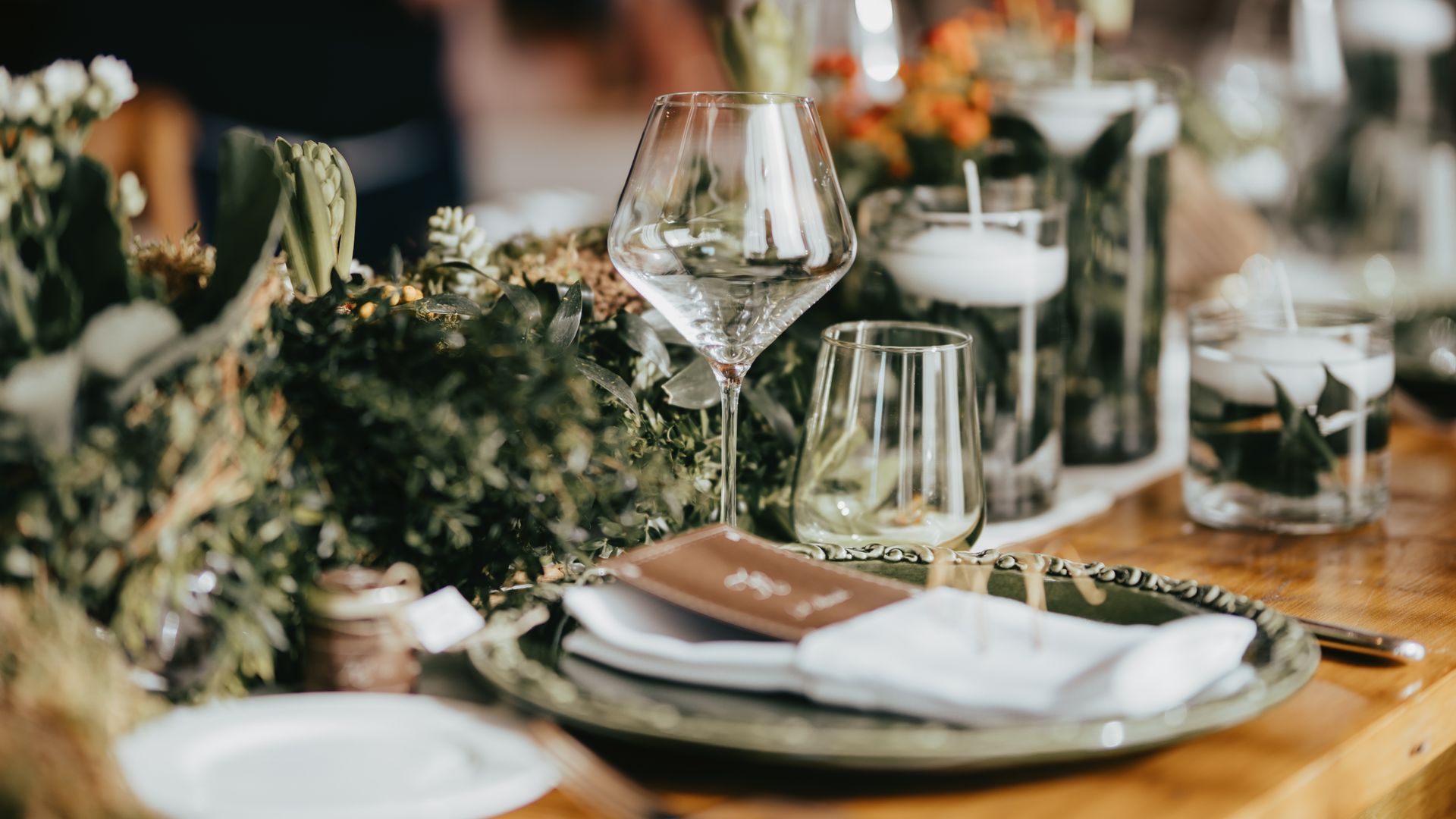 Elegant table setting with greenery, glassware, and place setting at an outdoor event.