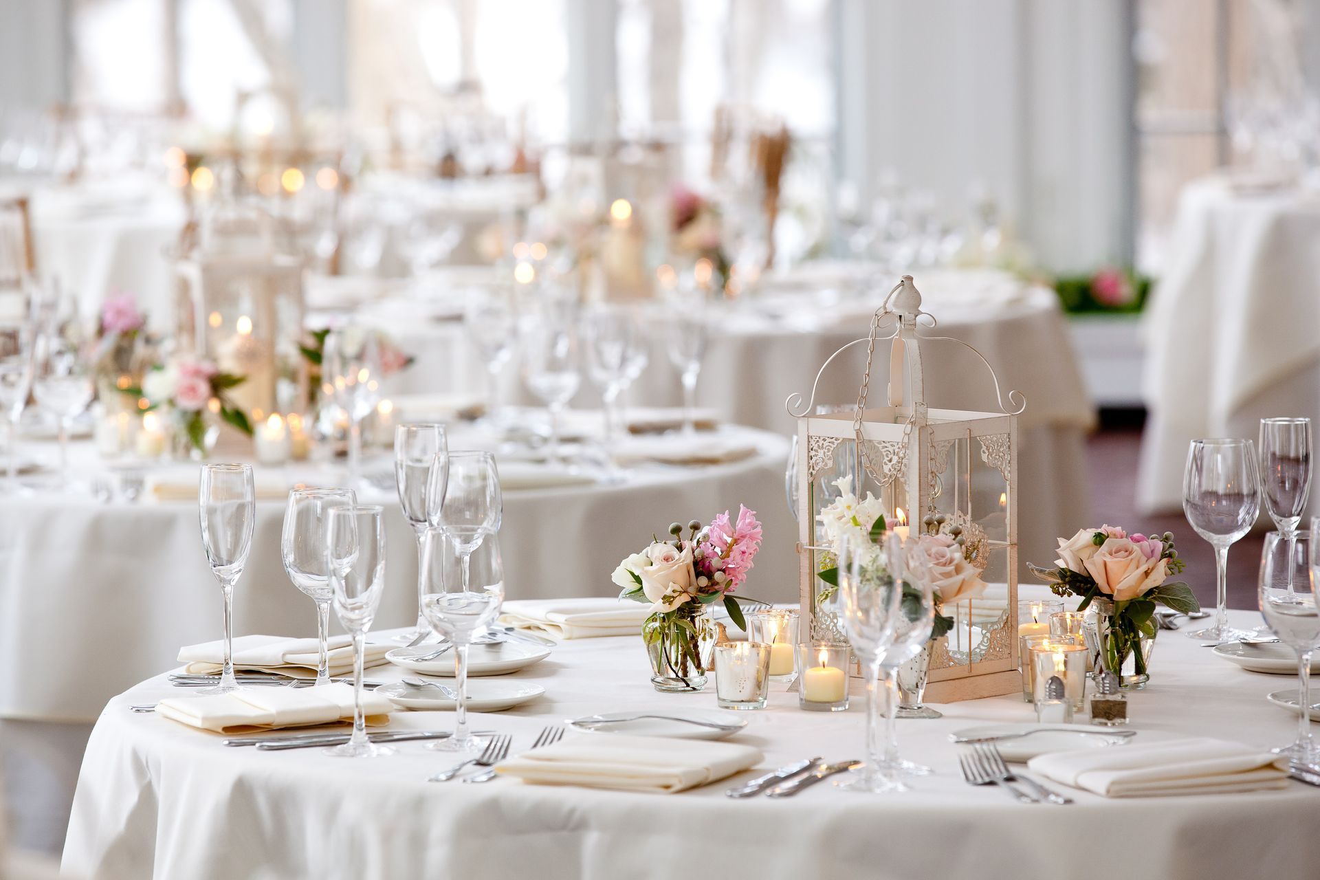 Wedding reception tables with white linens, floral arrangements, and glassware.