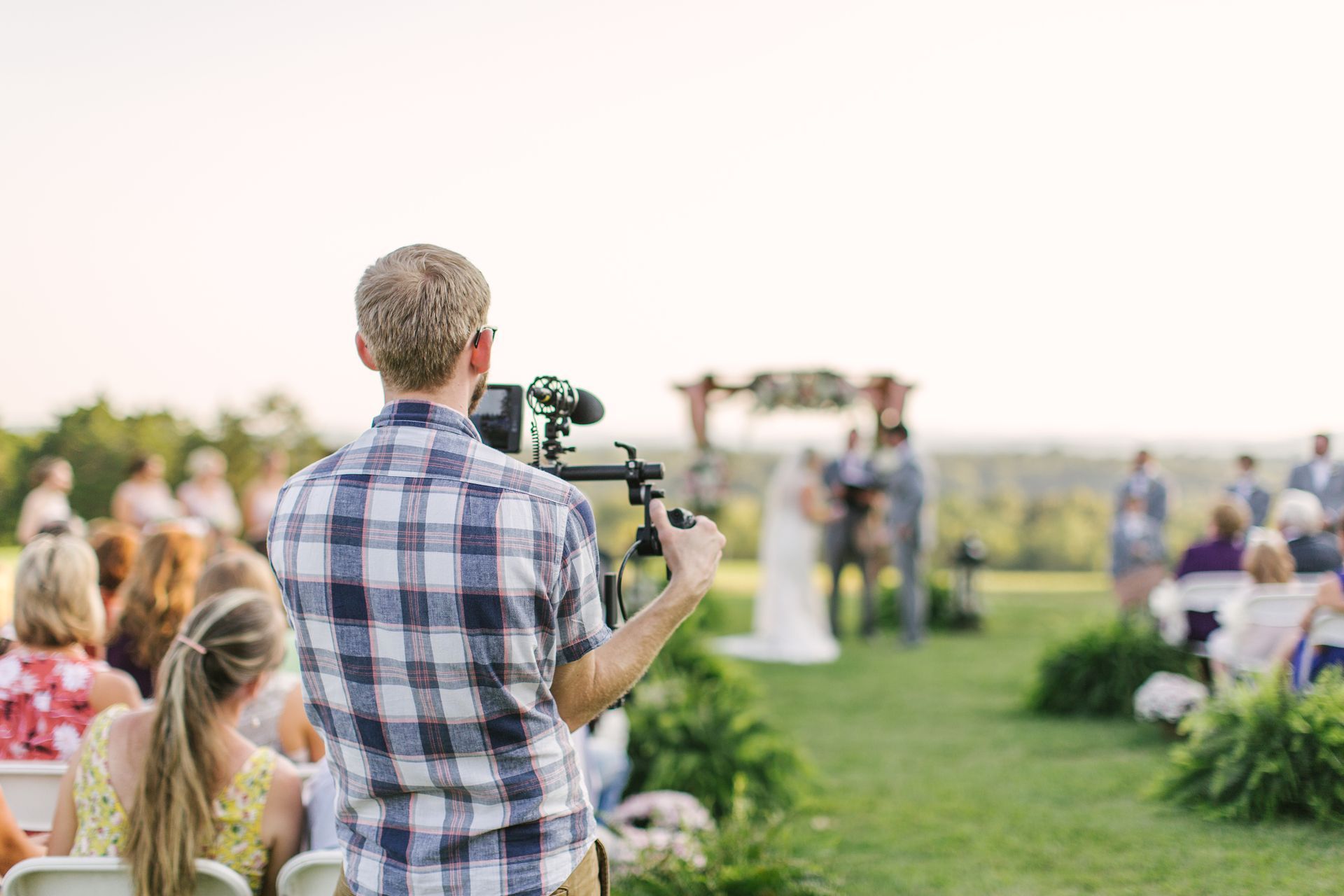 Videographer films wedding ceremony outdoors on a sunny day.