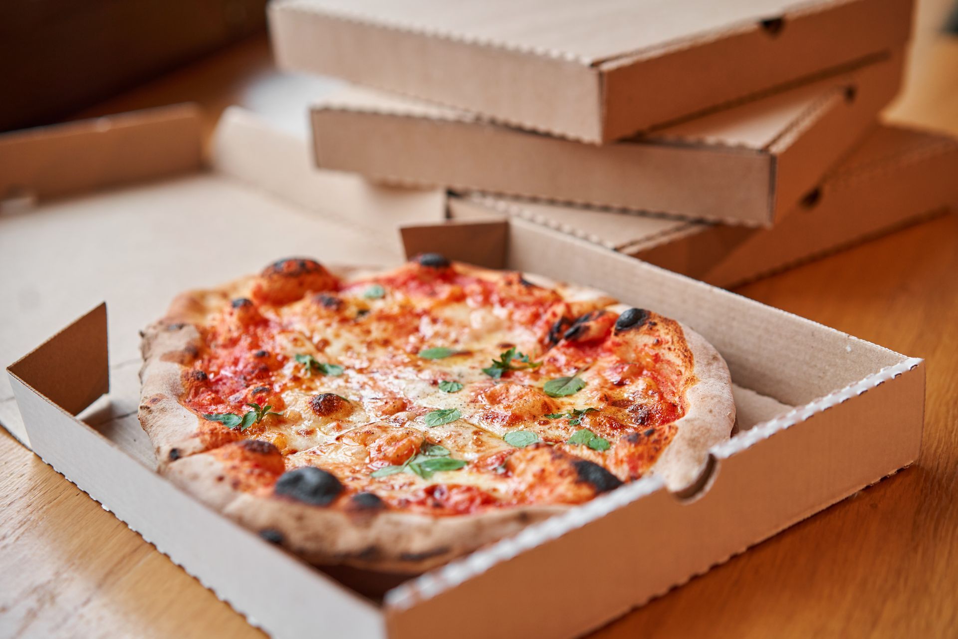Pizza in an open cardboard box with more boxes stacked in the background.