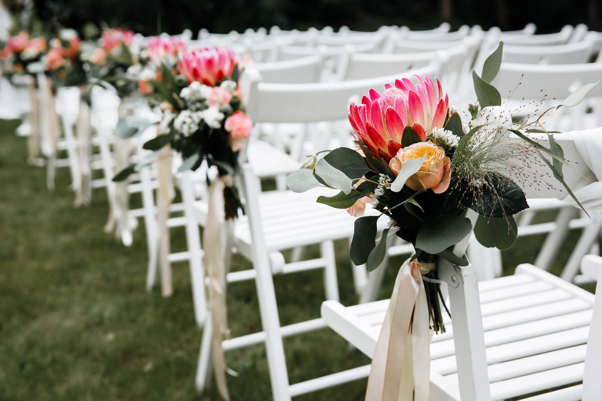 A row of white folding chairs decorated with flowers for a wedding ceremony.