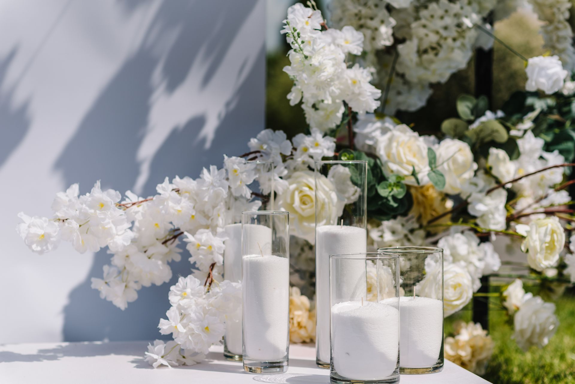 White flowers and candles decorate a white table; floral backdrop.