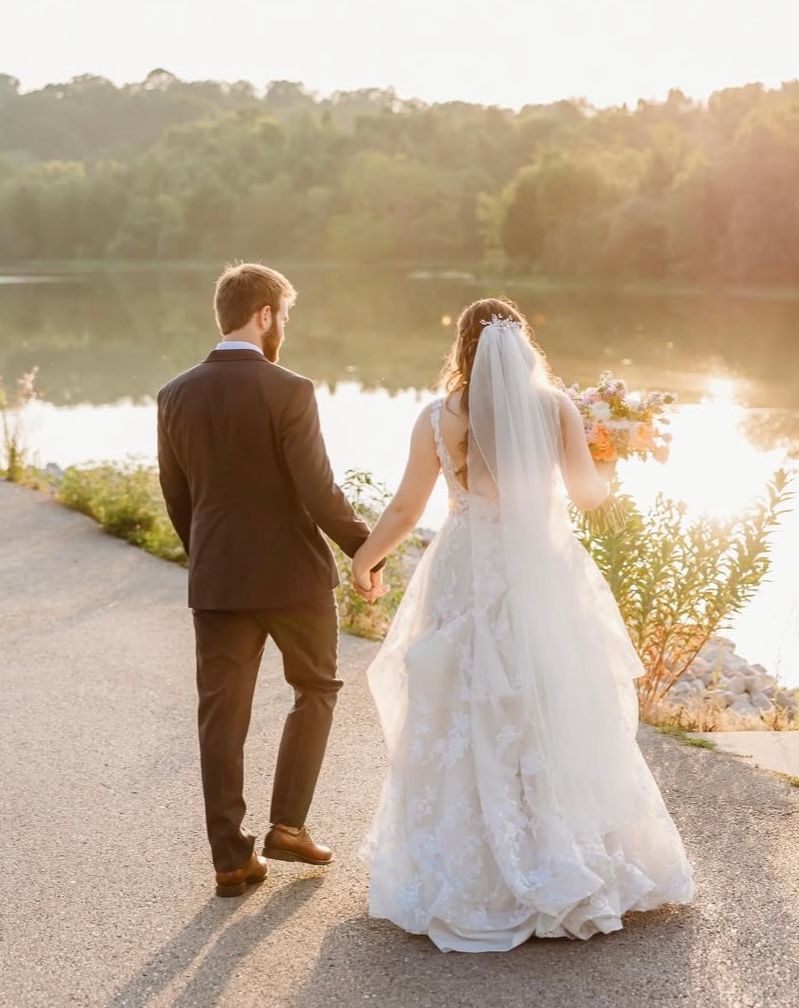 Newlyweds holding hands on a lakeside path at sunset at an outdoor wedding in Crittenden, Kentucky