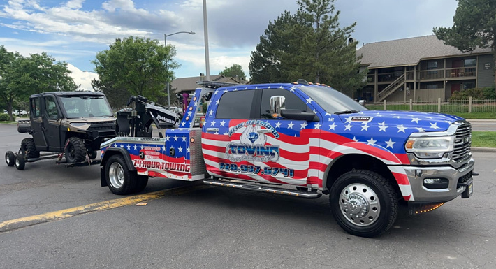 A tow truck with an American flag design towing a UTV.