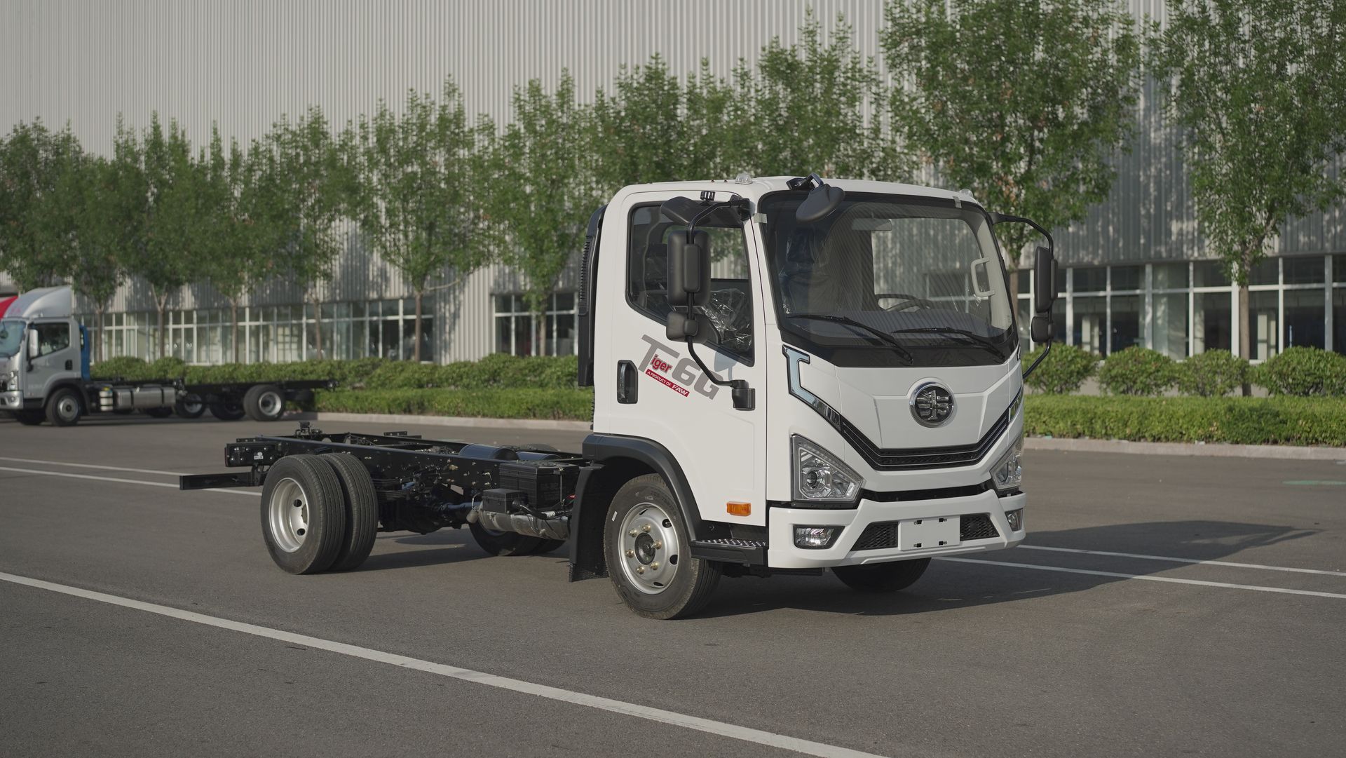 Un camión con chasis de cabina blanca estacionado en un terreno asfaltado frente a un moderno edificio de almacén.