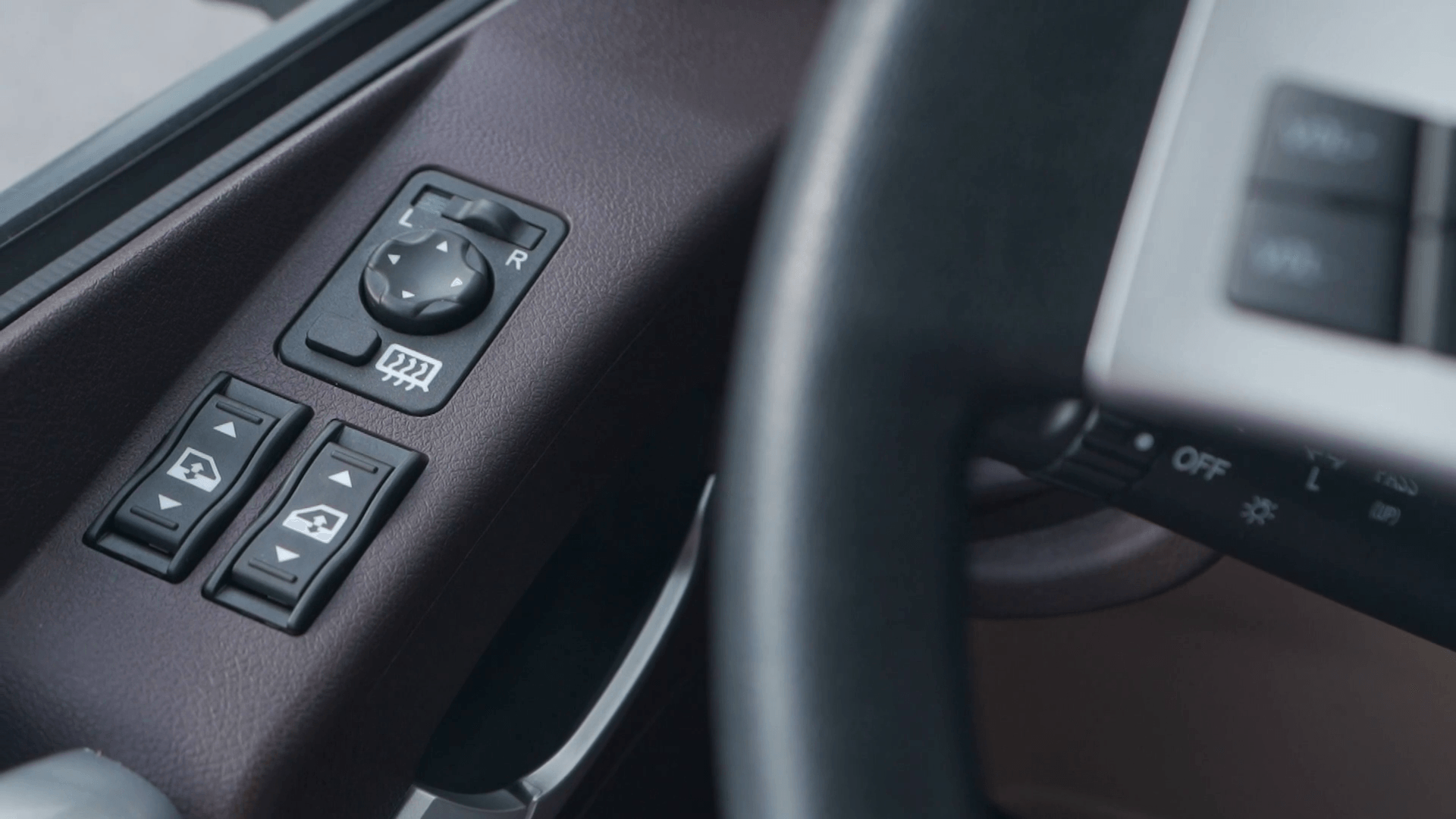 Un primer plano del panel de control de una puerta de automóvil con un volante en el fondo.