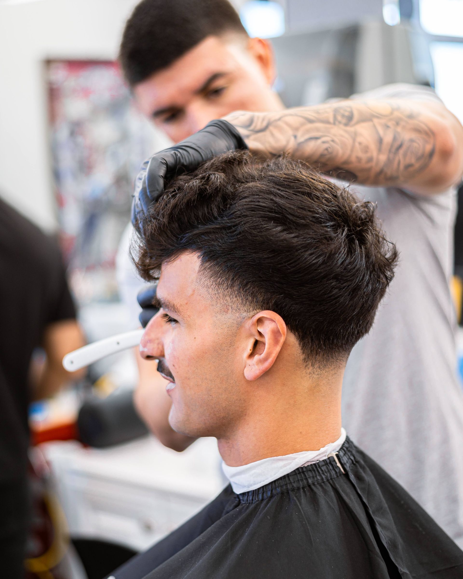 Barber trimming a client’s dark hair in a salon, with a fade haircut in progress