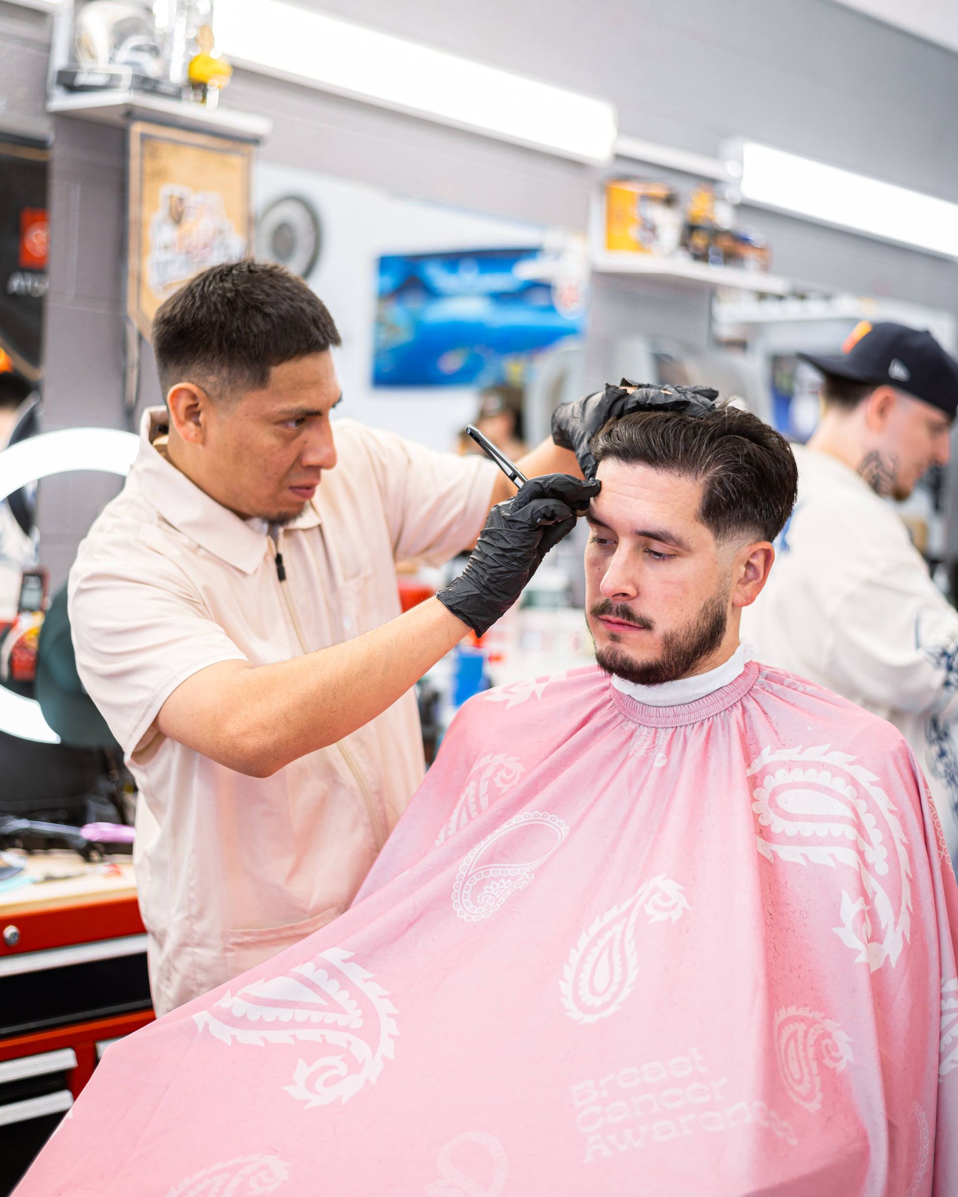 Barber trimming a client’s hair in a bright barbershop, client wearing a pink cape