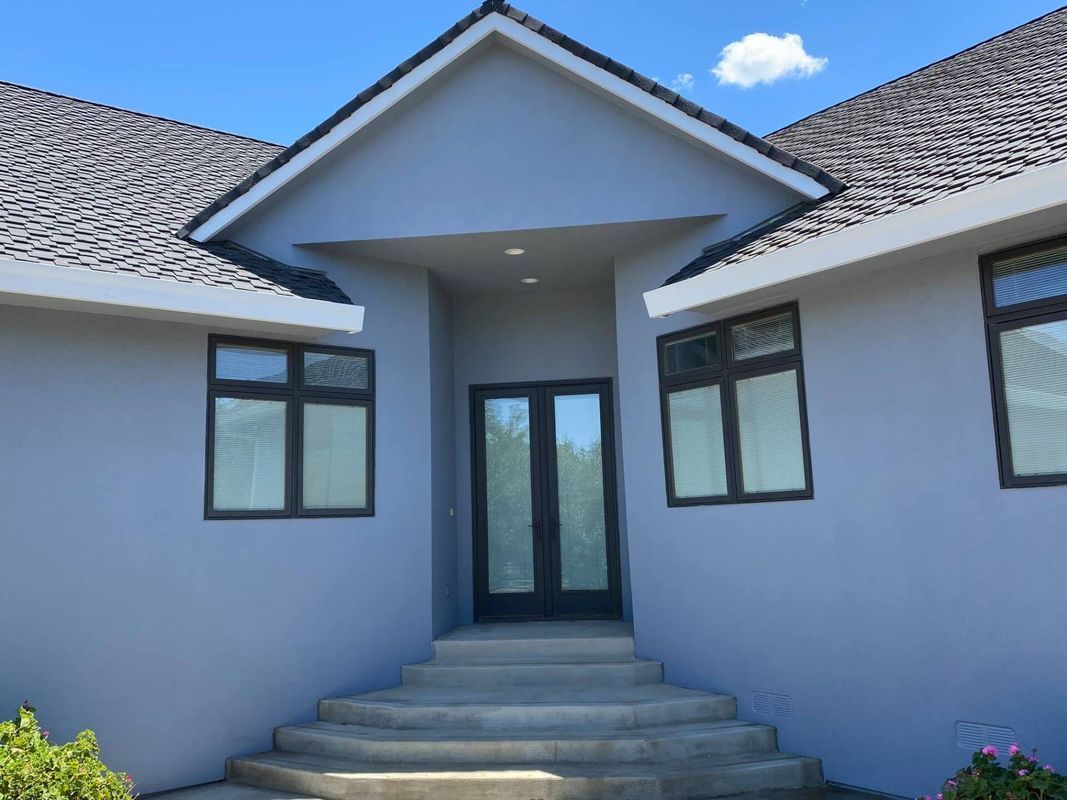 Gray house with dark-framed windows, double doors, and a set of concrete steps leading to the entrance.