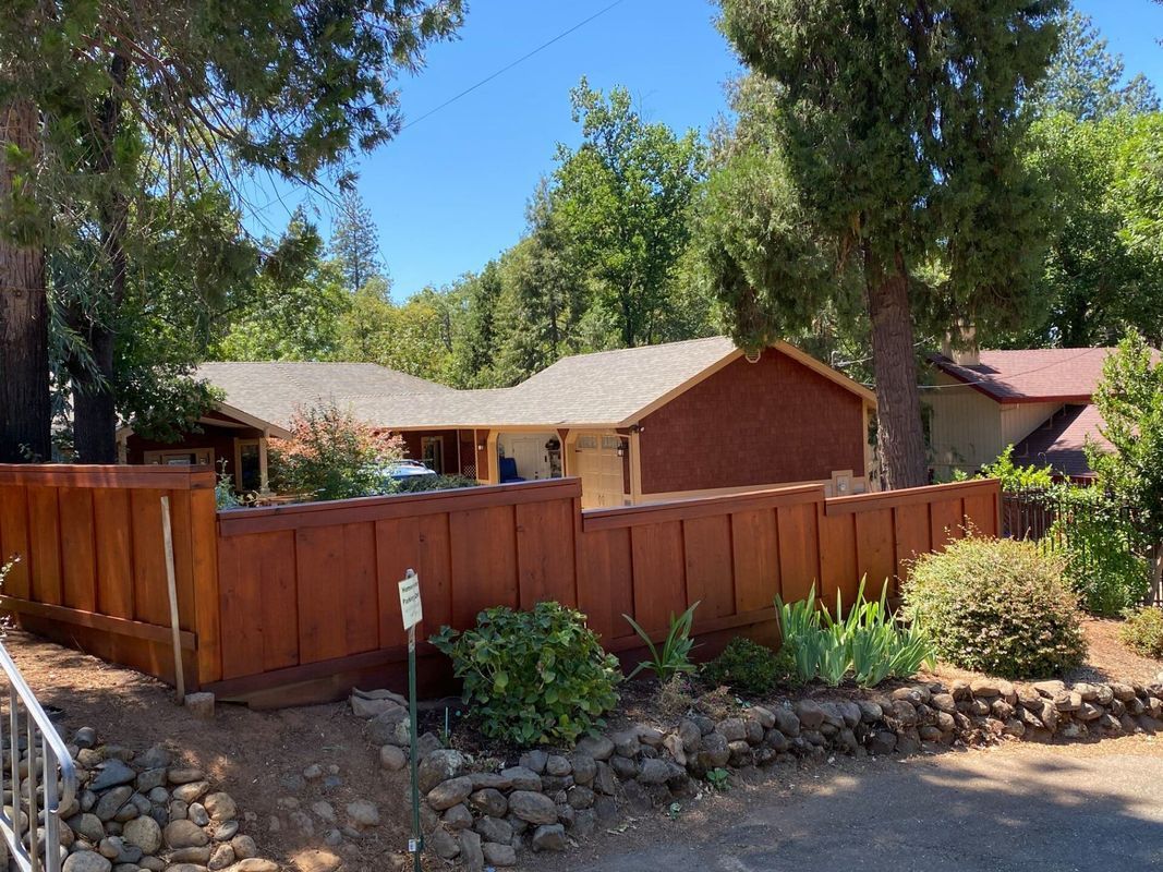 Brown house with a matching fence surrounded by trees under a blue sky.