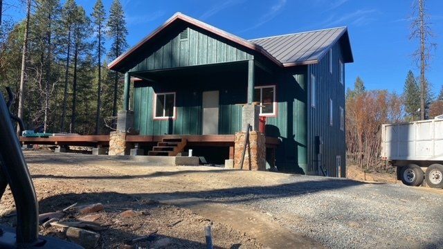 Green cabin with metal roof in a clearing, with a truck on the right.