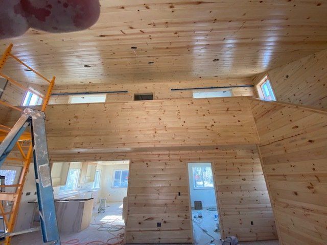 Interior of a wooden cabin under construction with a loft, showing natural wood walls and ceiling.