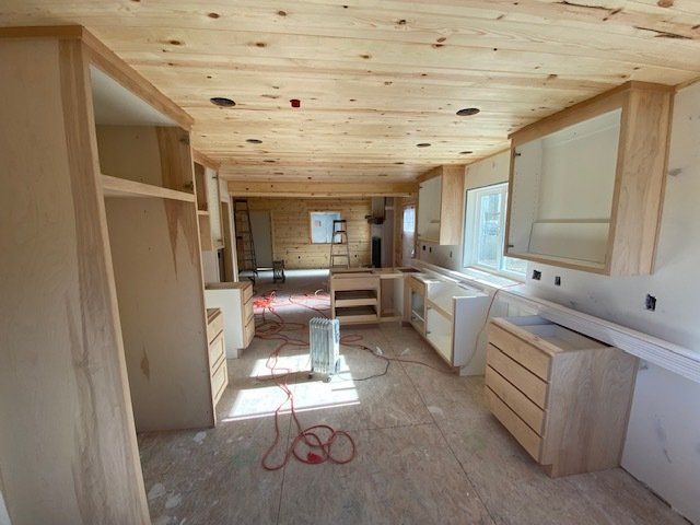 Interior of a kitchen under construction with light wood cabinets, ceiling, and walls.