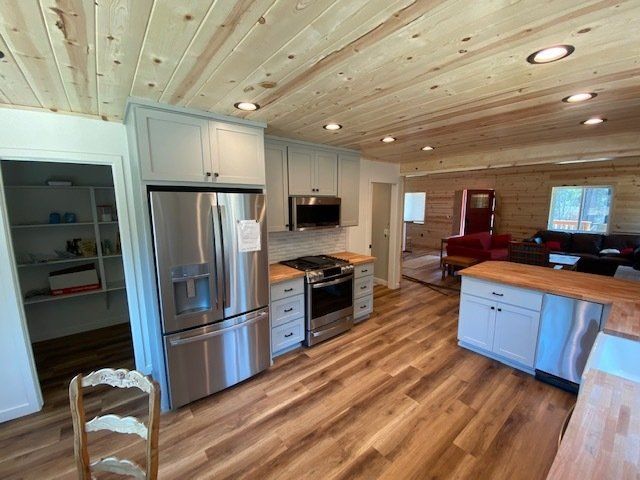 Kitchen with stainless steel appliances, light blue cabinets, wood countertops and flooring. Wooden ceiling.
