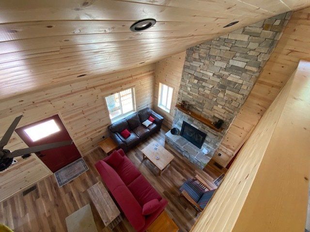 Interior view of a cabin living room with stone fireplace, wooden walls, and two couches.