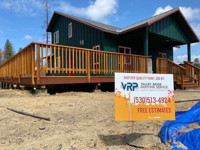 A house with a green exterior and wooden deck. A sign for Valley Ridge Painting Service is in front.