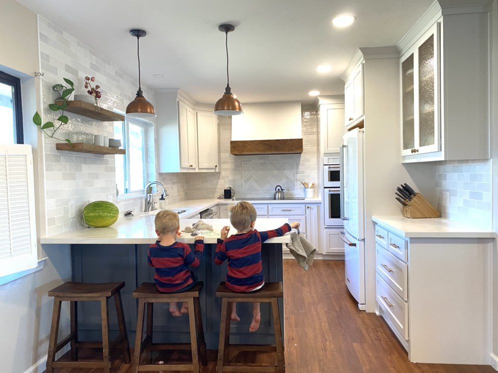 Two children seated at a kitchen island, reaching towards the counter, in a bright kitchen.