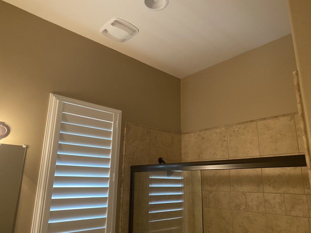 Bathroom interior with tan walls, shower, window with shutters, and ceiling fan.
