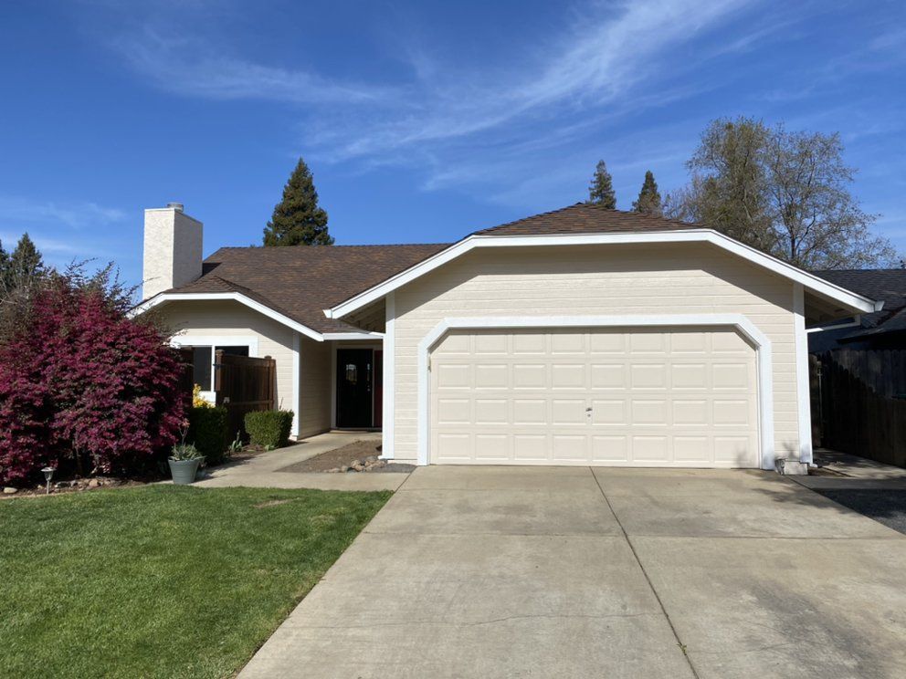 Beige suburban house with a brown roof and a two-car garage under a blue sky.