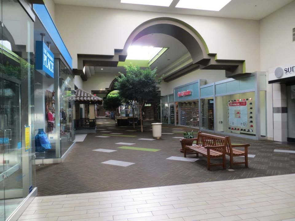 Interior of a mostly empty mall with shops, benches, and a skylight.