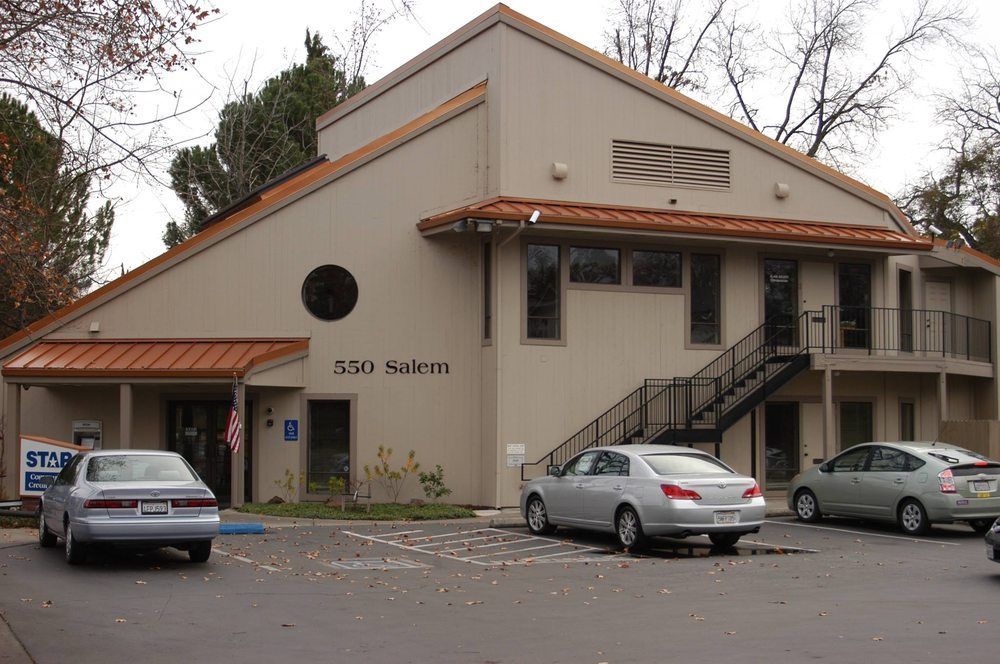 Tan office building with copper-colored awnings and three cars parked in front.