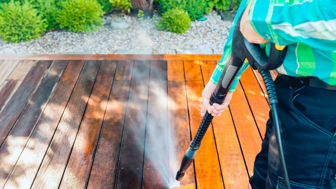 Person pressure washing wooden deck, cleaning half of the planks, showing the before and after effect.
