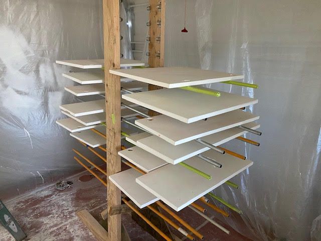 Painted white panels drying on a rack in a room covered in plastic sheeting.