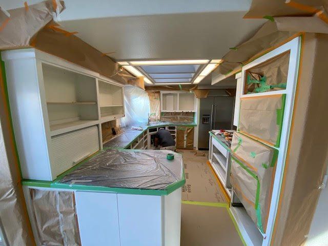 Kitchen renovation: Cabinets, appliances, and countertops covered in protective materials, ready for painting.