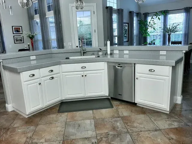 White kitchen cabinets with gray countertops, stainless steel dishwasher, and a window.