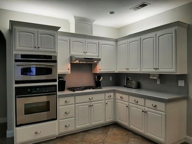 White kitchen cabinets with stainless steel appliances. Counters are gray with a tile floor.
