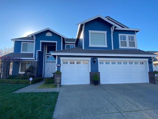 Blue two-story house with white trim and garage doors, set against a clear blue sky.