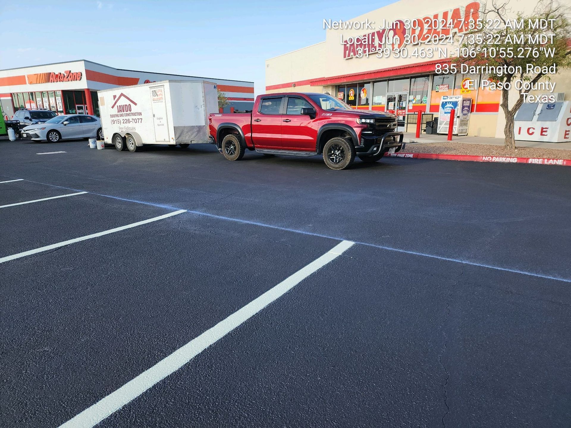 A red truck is parked in a parking lot next to a store.