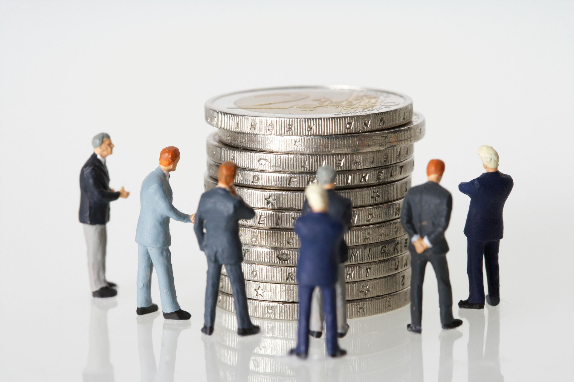 Miniature figures of business people surrounding a stack of coins.