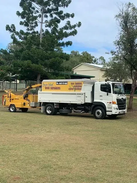 A white truck with a yellow wood chipper on grass next to trees — Boyne Island Tree Services in Boyne Island, QLD