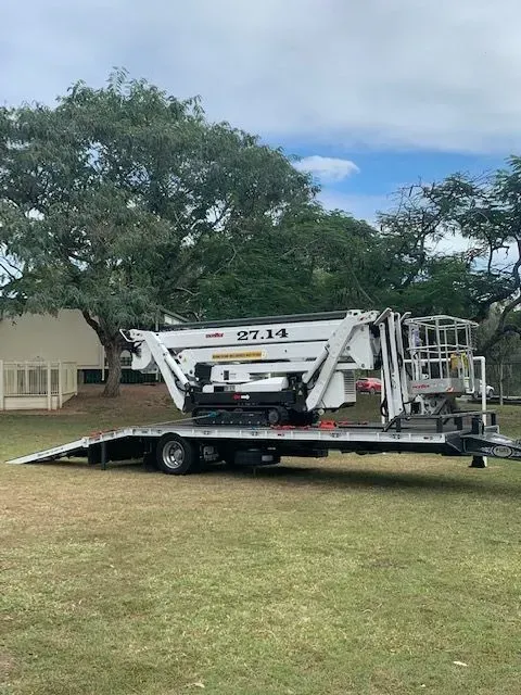 White aerial lift on a trailer in a grassy area, trees in the background — Boyne Island Tree Services in Boyne Island, QLD