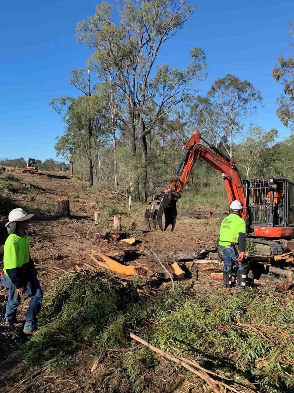 A Group of Men Are Standing in A Field Next to A Large Excavator — Boyne Island Tree Services in Boyne Island, QLD