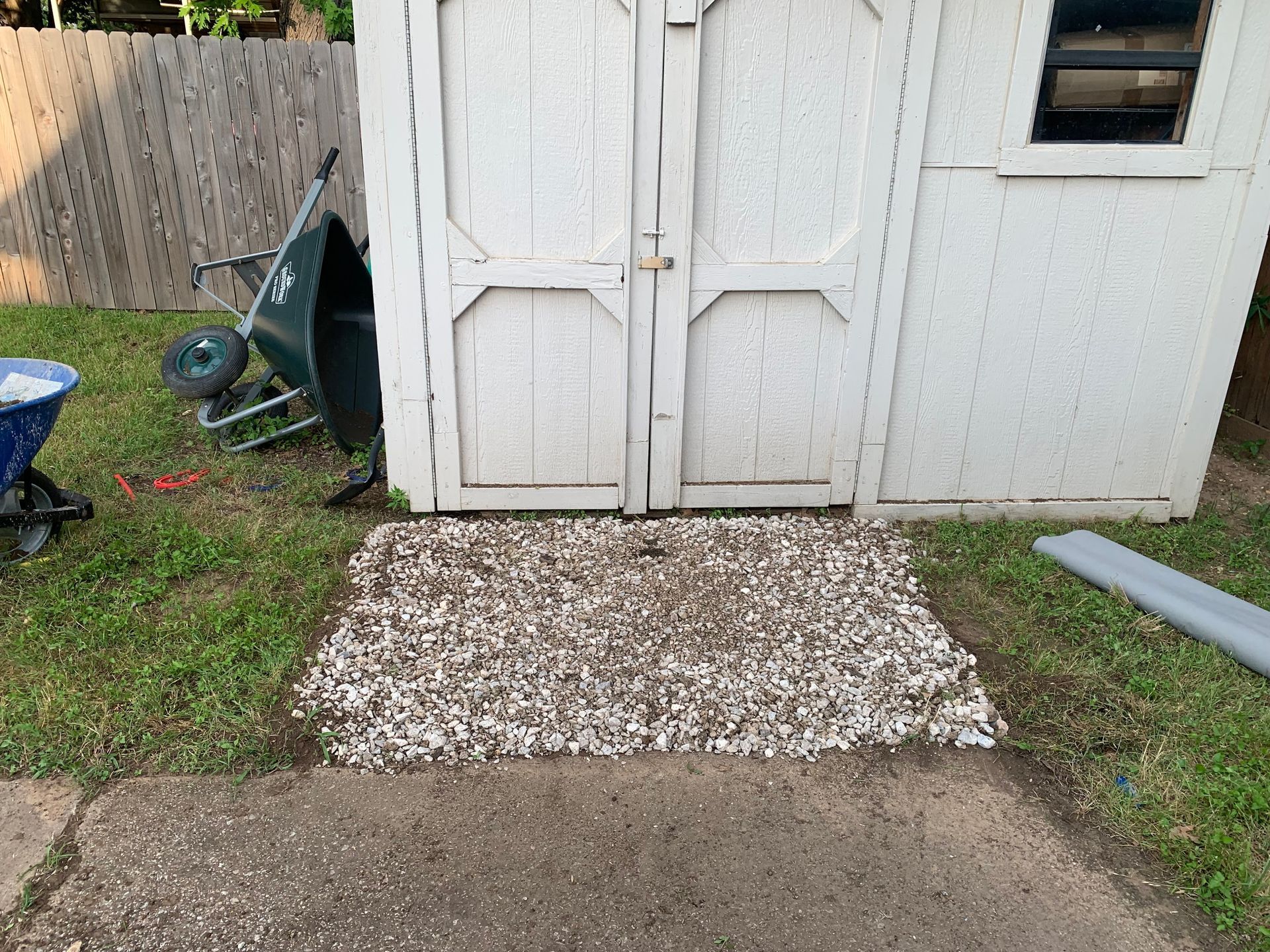 A white shed with a wheelbarrow in front of it.
