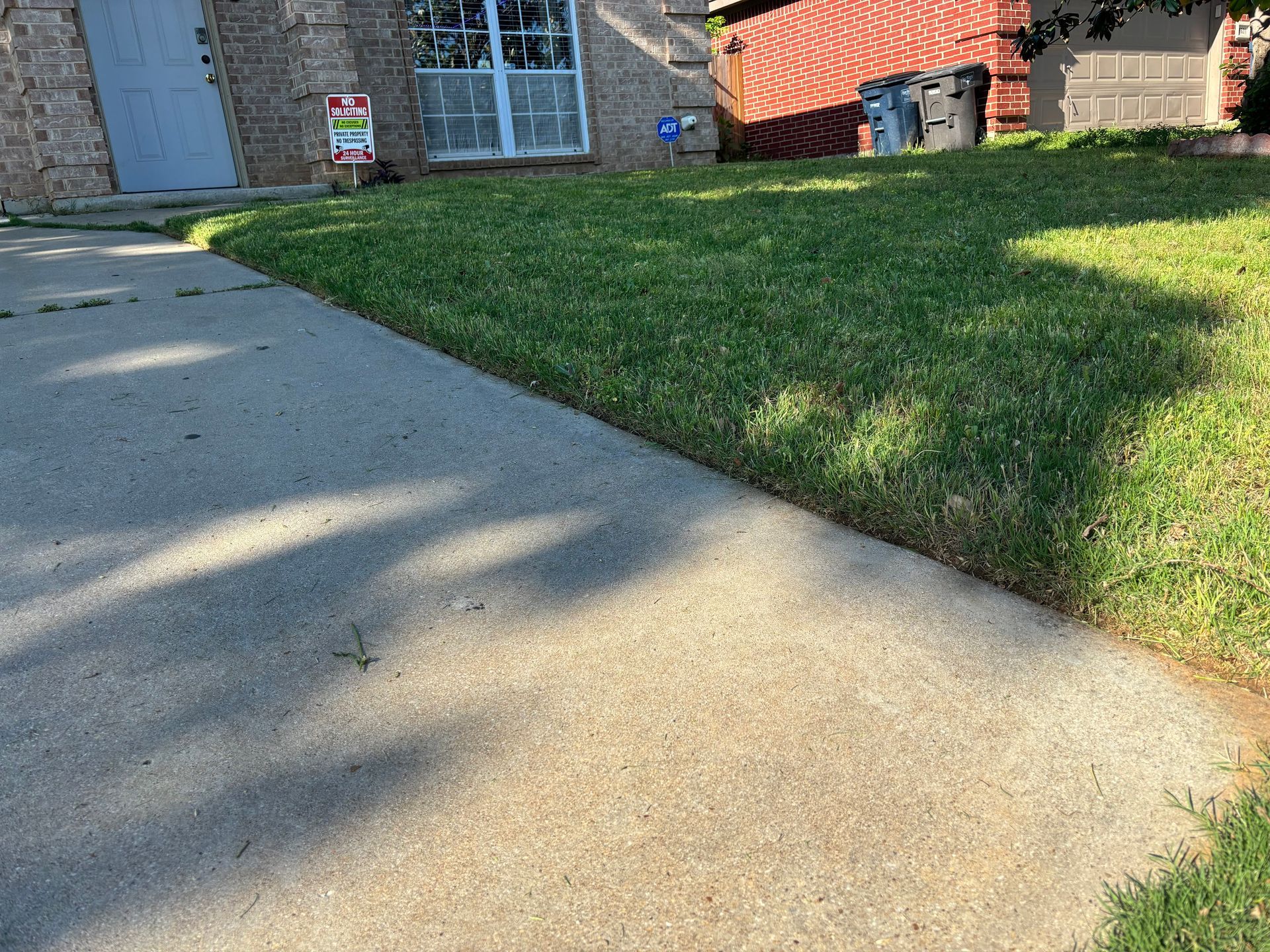 A concrete sidewalk next to a lush green lawn in front of a brick house.