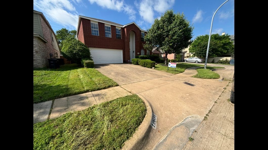 A red brick house with a white garage door is for sale in a residential area.