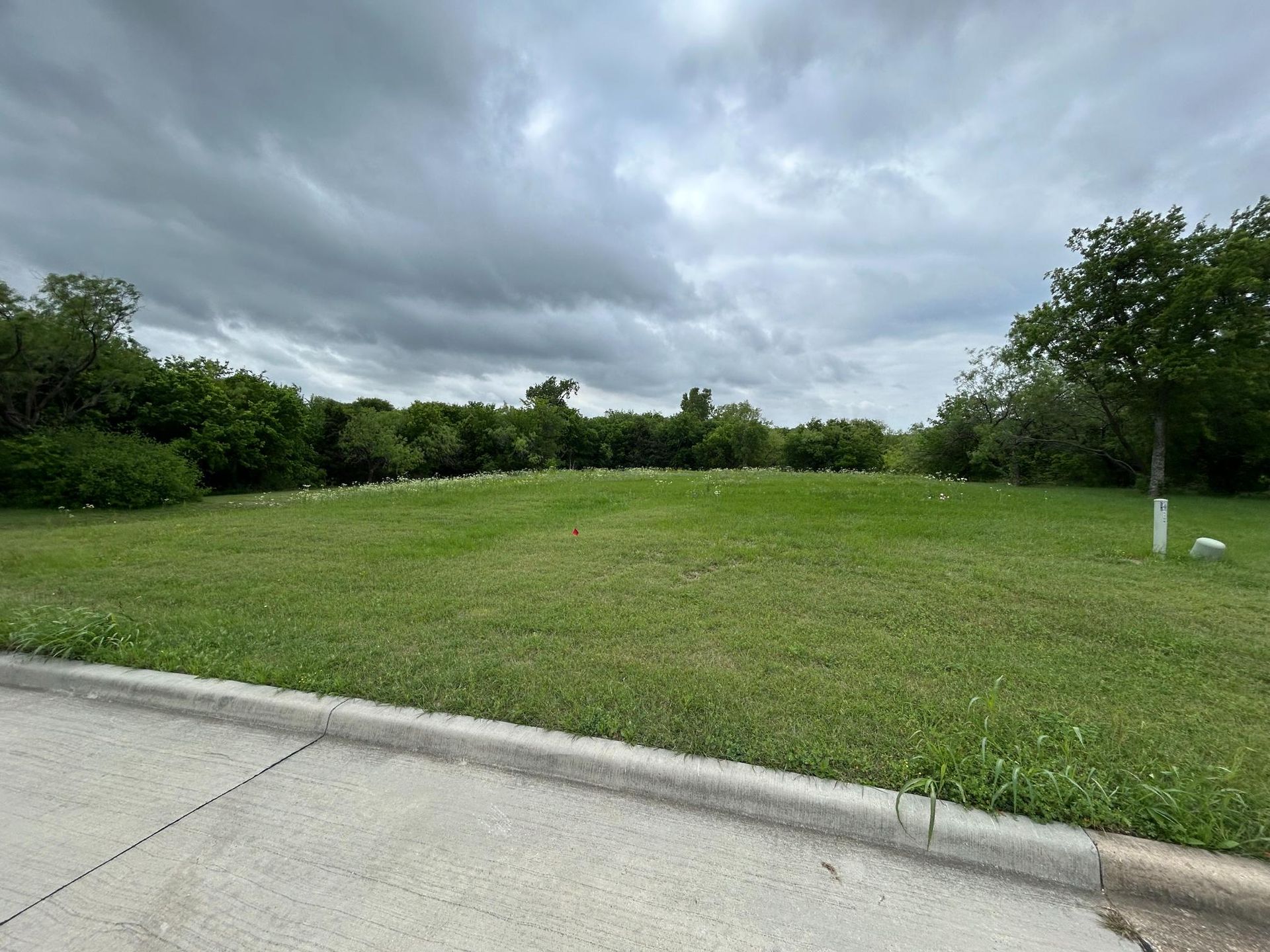 Empty grassy lot beside a sidewalk under cloudy skies