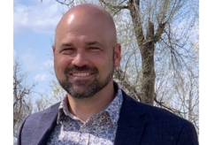 A bald man with a beard is wearing a suit and smiling.