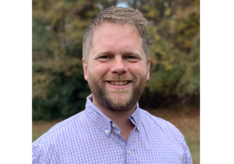 A man with a beard is wearing a plaid shirt and smiling for the camera.