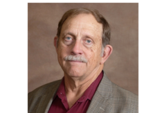 A man with a mustache is wearing a suit and a red shirt.