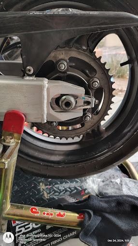 Close-up of a scooter/motorcycle rear wheel and exposed chain drive with silver engine parts.