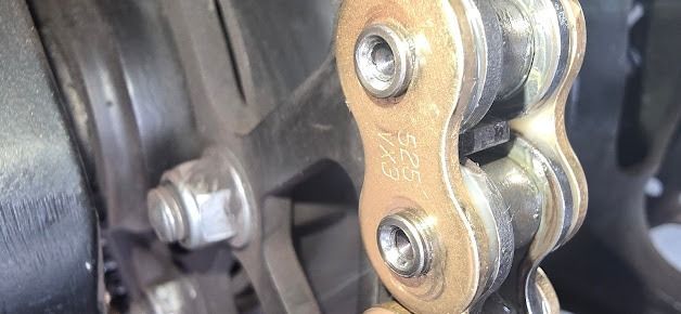 Close-up of a gold motorcycle chain and sprocket on a wheel assembly