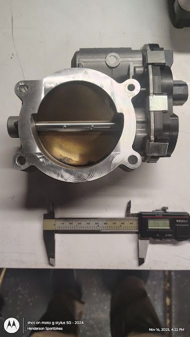 Close-up of a metal throttle body with a ruler beneath it for scale.